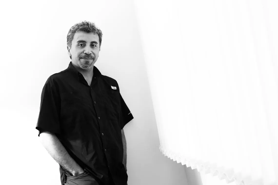 Retrato en blanco y negro de Edgard Garrido, apoyado en una pared blanca con las manos en los bolsillos.