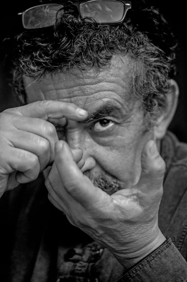 Retrato en blanco y negro de Héctor González de Cunco, con los lentes sobre la cabeza, forma un visor con los dedos frente a su ojo.