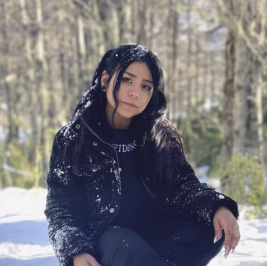 Retrato en blanco y negro de Nicole Kramm, sentada en la nieve en un bosque, con chaqueta oscura.