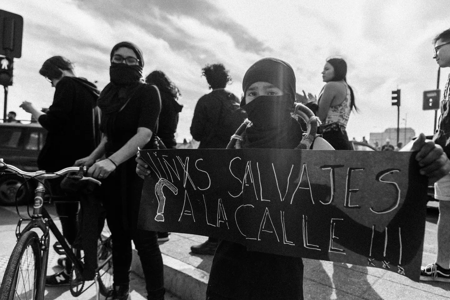 Foto de Alexandra Pinto: una persona con el rostro cubierto sostiene un cartel que dice Niñxs salvajes a la calle.